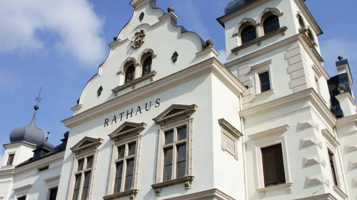 White Rathaus (town hall) façade with decorative gables, arched windows, and a tall tower against a blue sky, European architectural detail